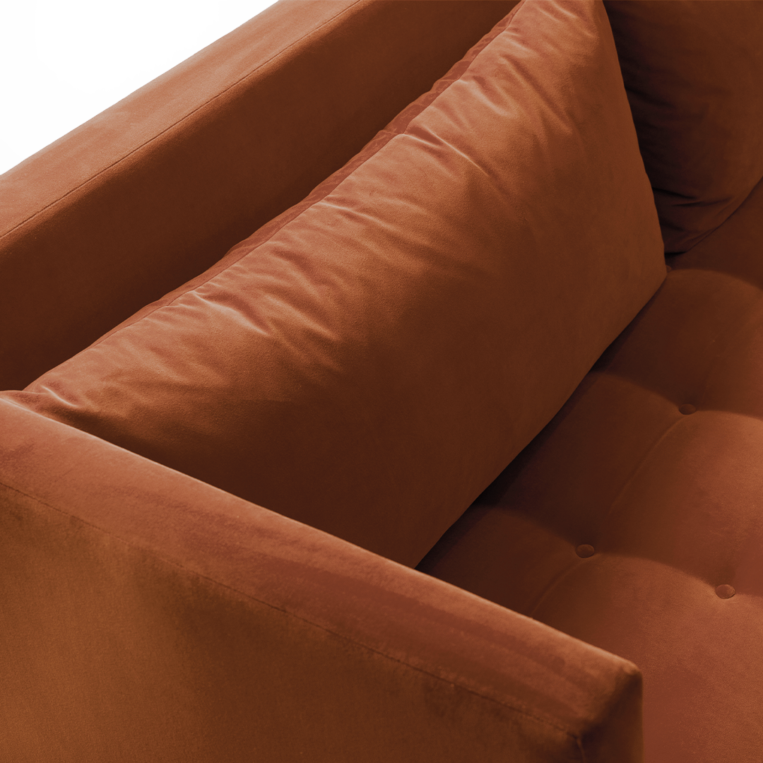 Speaker - detaljbild på roströd soffa med dekorativa knappar i sits och lösa ryggkuddar.