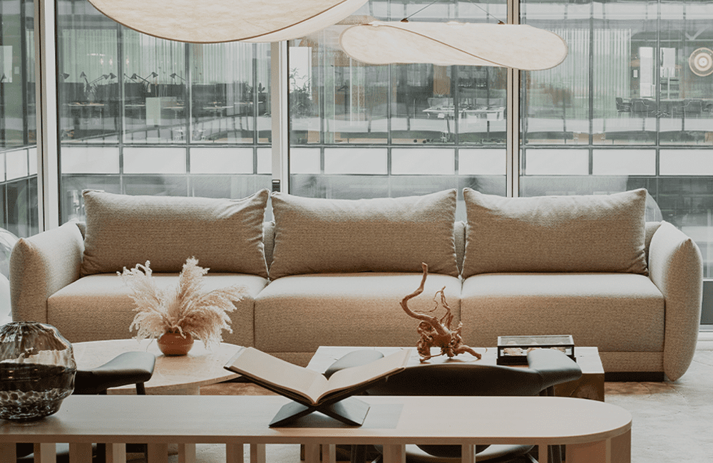 Miljöbild på soffan Arena - en stilren 3-sitssoffa med spännande design. Soffan har höga smala armstöd, elegant formspråk och härlig komfort. Klädd i ett beige tyg.