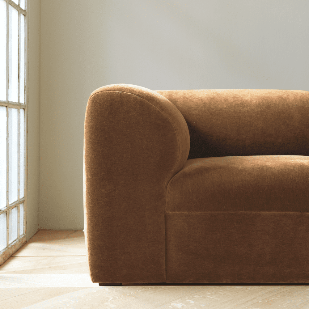 Detaljbild på soffan Ginos armstöd. Mjuka, runda former. Klädd i ljusbrun sammet.